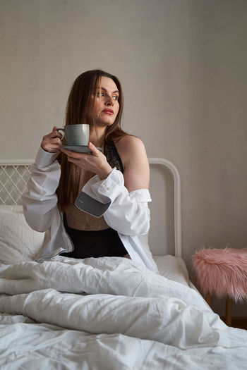 Young woman drinking coffee while sitting on bed at home