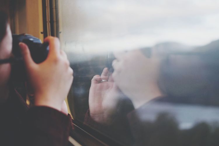 Cropped image of man photographing through camera while sitting in train