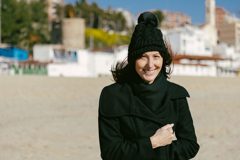 Smiling woman in hat and coat on the beach on a sunny winter day