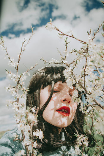 Close-up of woman with eyes closed by plants against sky