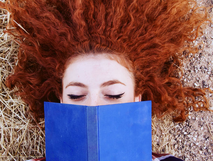 Directly above shot of redhead woman holding book while lying on field