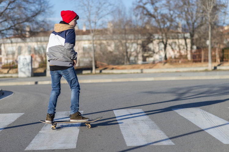 Rear view of boy skateboarding on road
