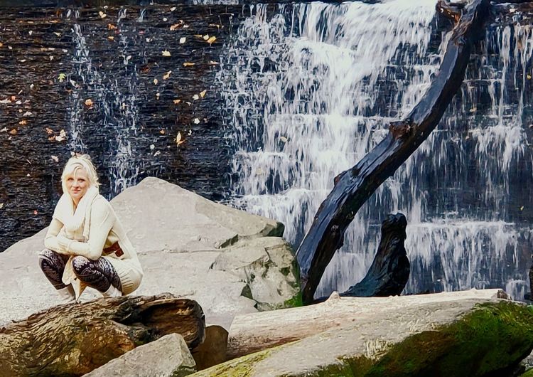Portrait of woman sitting on rock by waterfall