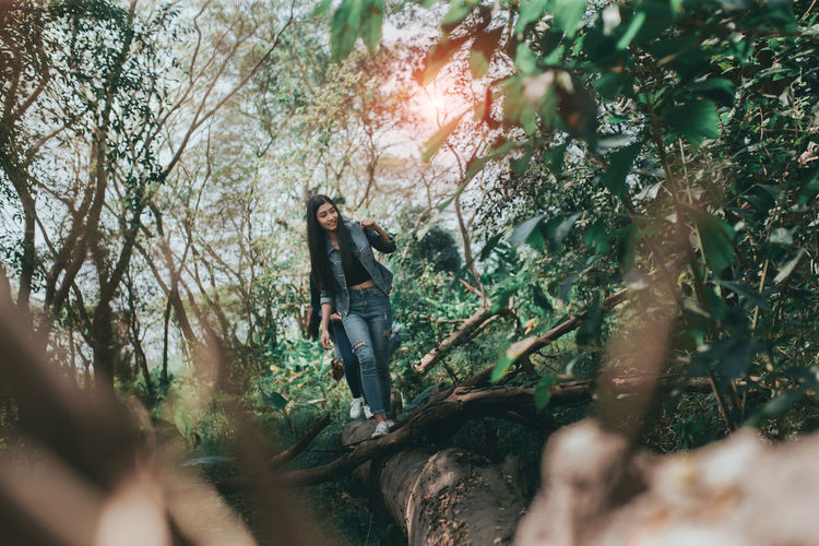 Full length of woman walking on fallen tree in forest
