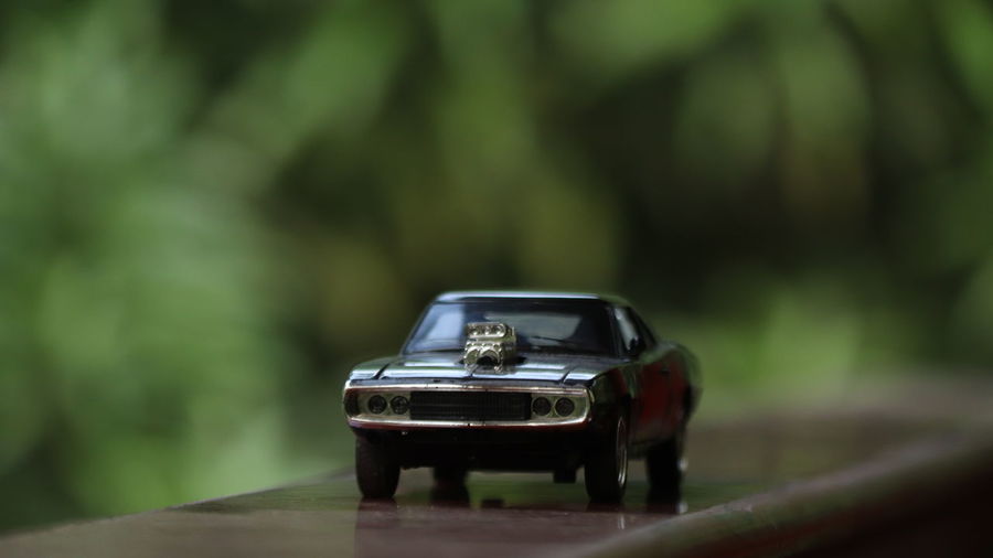A black die cast toy car on a greenery background.