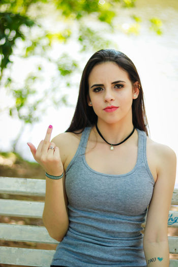 Portrait of young woman showing middle finger on bench