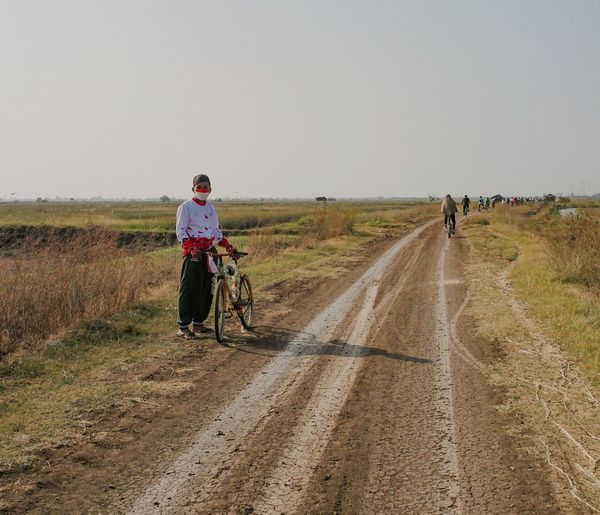 Man riding bicycle on dirt road against clear sky