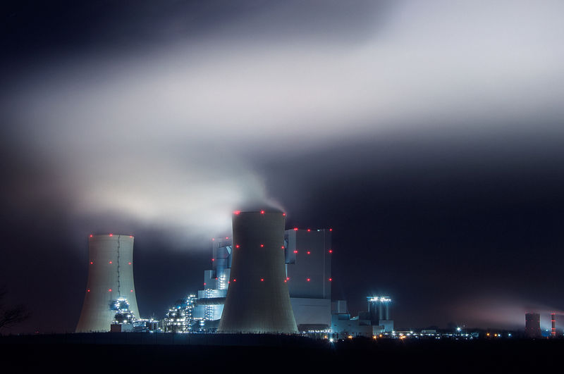 Panorama of coal power plant at night with smoke from cooling towers