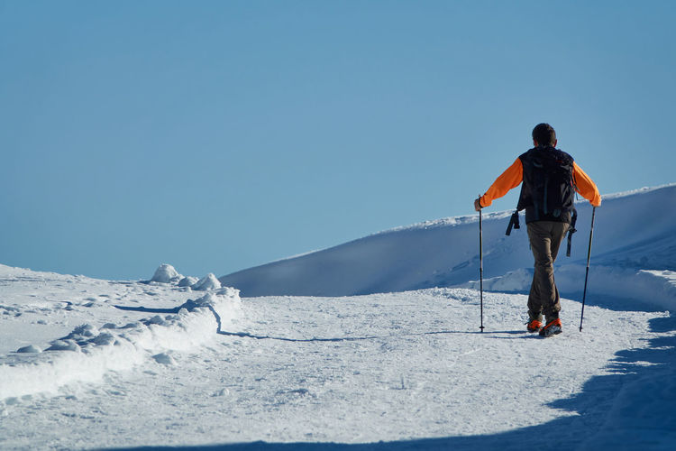 Man walking on snow with stick for nordic walkings and boots with crampons