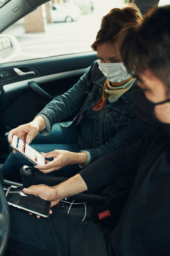 Woman wearing mask holding smart phone sitting at car