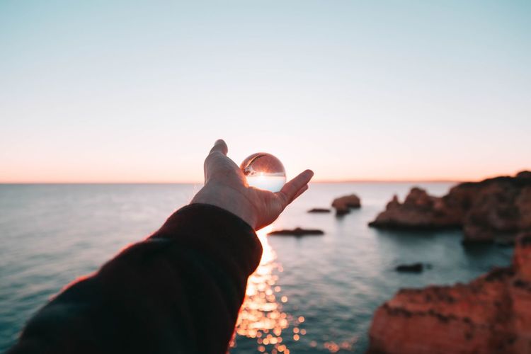 Cropped hand holding crystal ball against sea