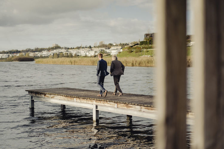 Two businessmen walking on jetty at a lake