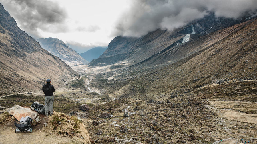 Rear view of man standing on mountain against cloudy sky