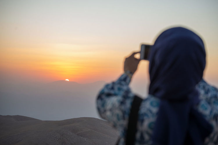 Rear view of woman photographing against sky during sunset