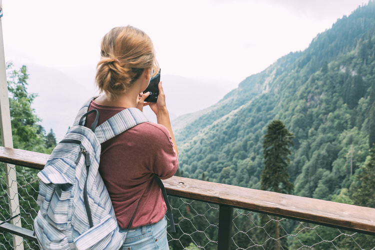 Young woman with a backpack in the mountains taking picture on camera of mobile phone. s