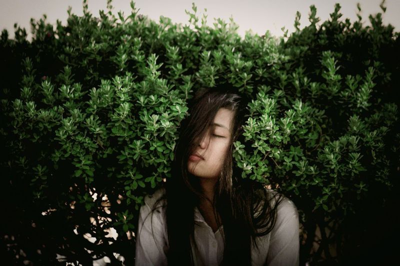Young woman with eyes closed sitting amidst plants