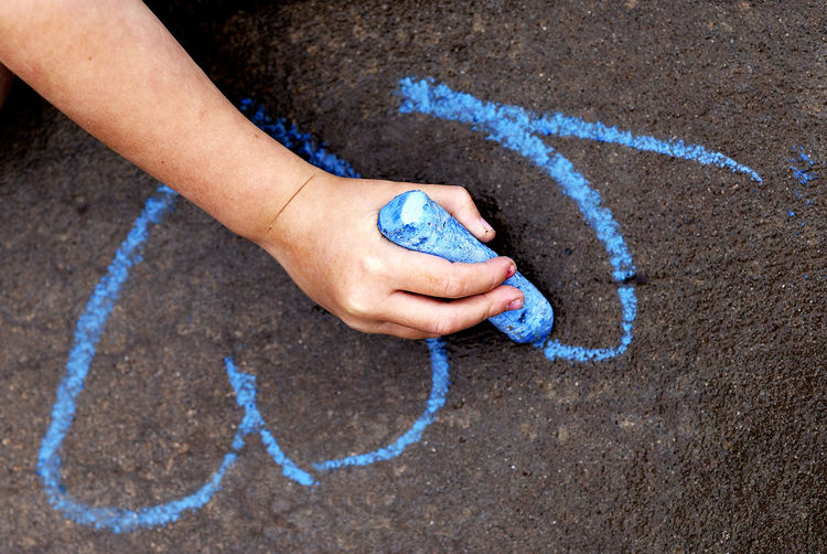 Low section of child drawing on ground with chalk