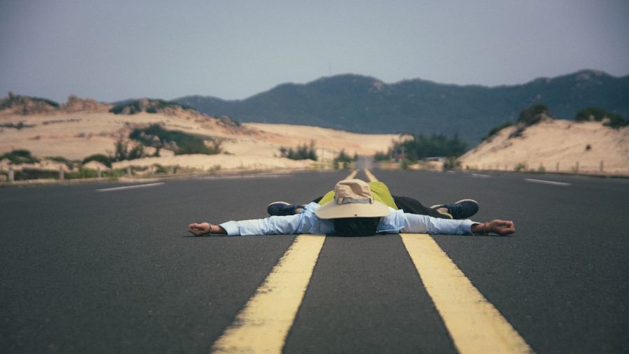 Man with arms outstretched lying on road against clear sky