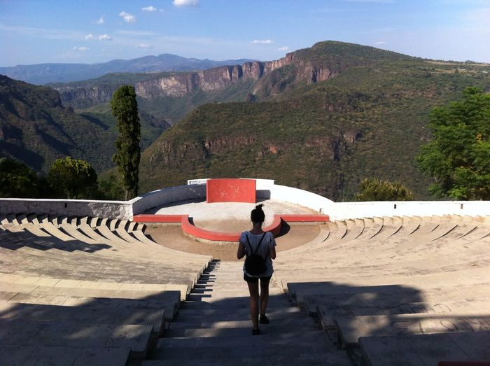 Rear view of woman moving down steps at amphitheater against mountains