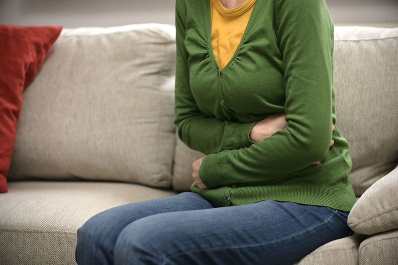 Midsection of woman suffering from stomached sitting on sofa at home