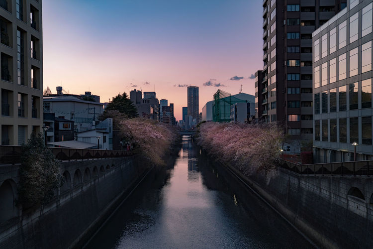 Canal amidst buildings in city against sky during sunset