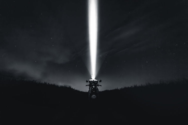 Silhouette man with illuminated flashlight against sky at night