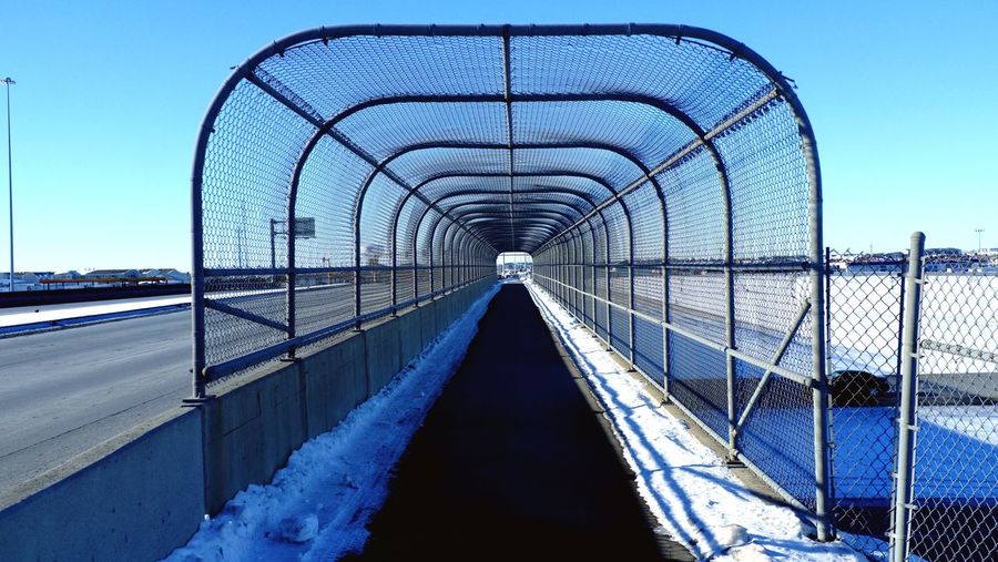 Walkway covered with metal fence against sky during winter