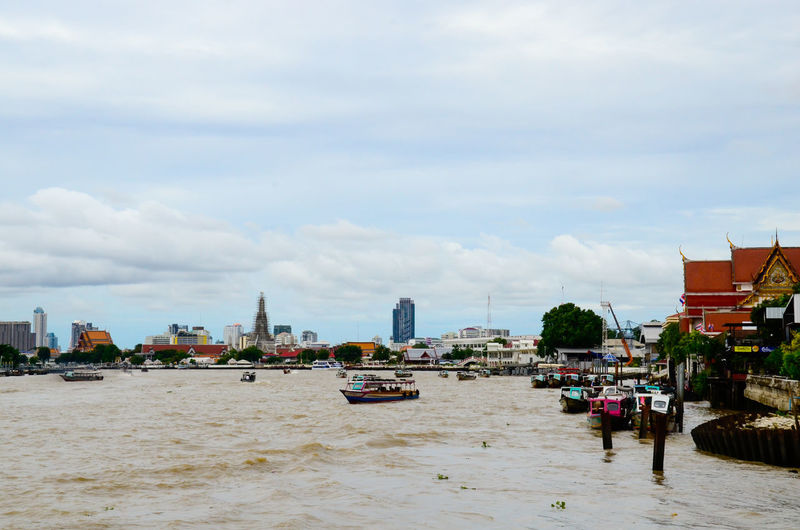 Boats on chao phraya river against cloudy sky