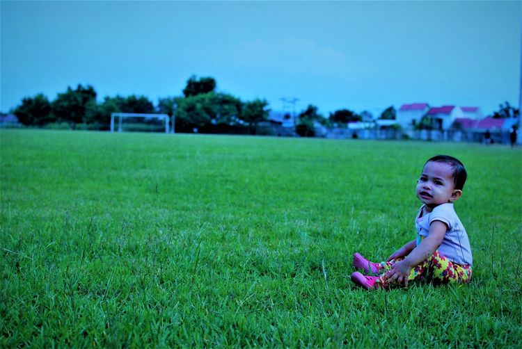 Full length of girl looking away while sitting on grass