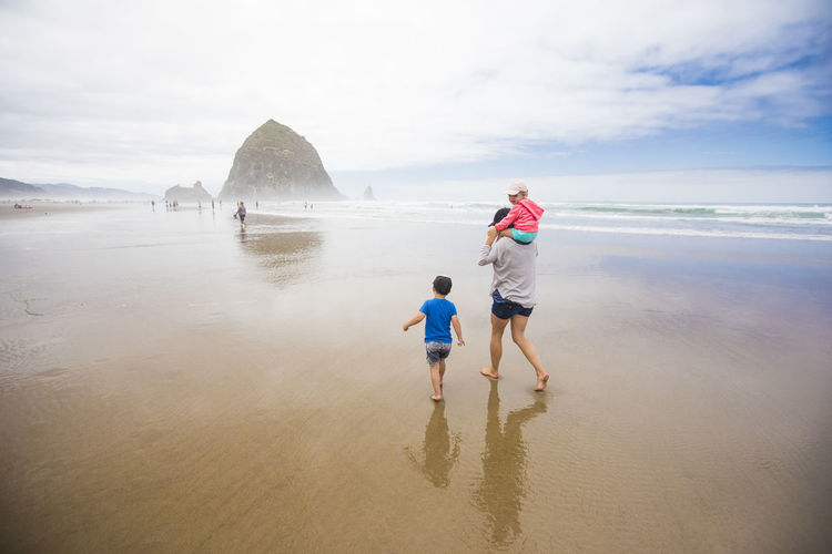 Mother and two kids walk toward haystack rock, cannon beach.