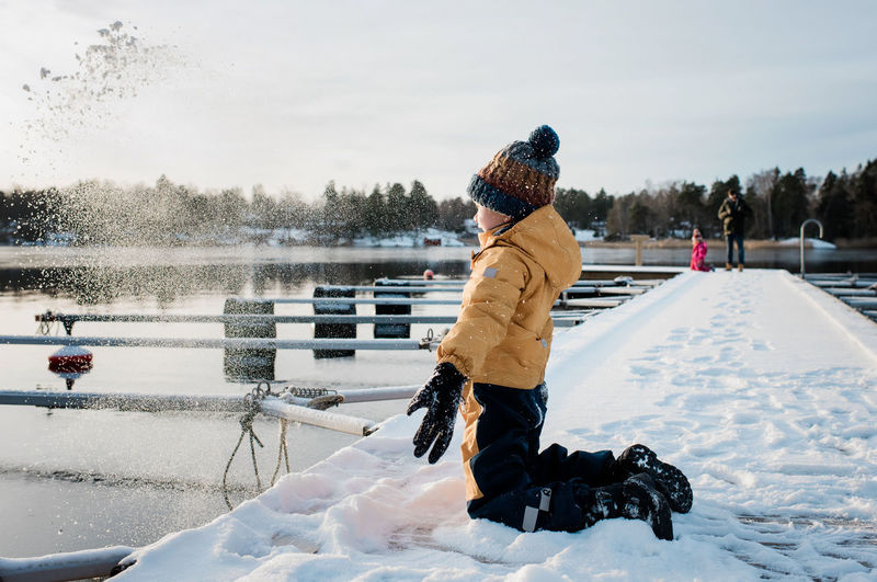 Boy throwing snow up in the whilst playing outside by the sea