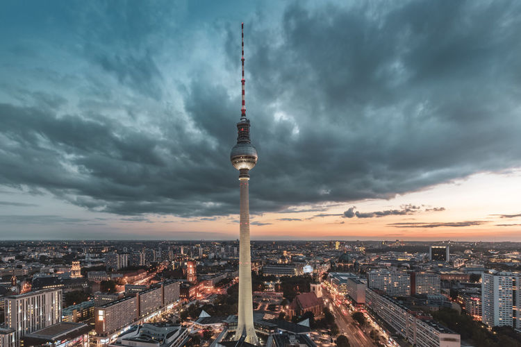 Communications tower in city against cloudy sky during sunset