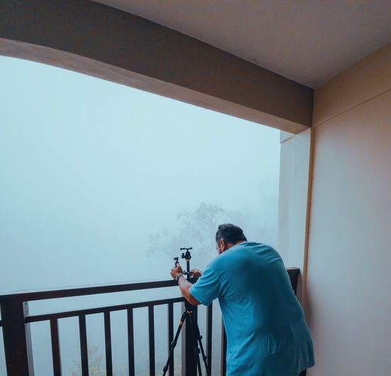 Investigator or private detective setting tripod for taking photo from balcony of a building.