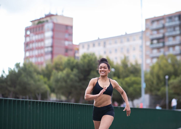 Focused african american female athlete in sportswear running along path in urban park during training in summer