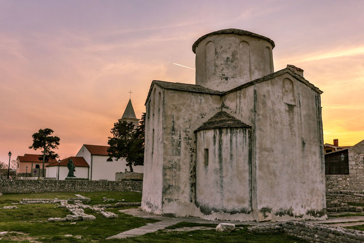 Exterior of old church on field against sky during sunset