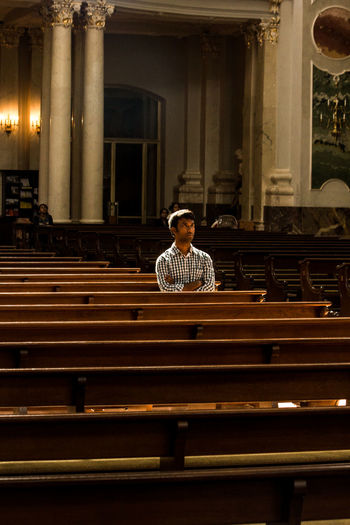 Man with arms crossed sitting on bench in church