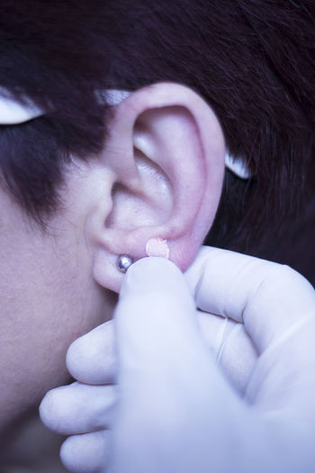 Cropped hand of doctor holding adhesive bandage on person ear