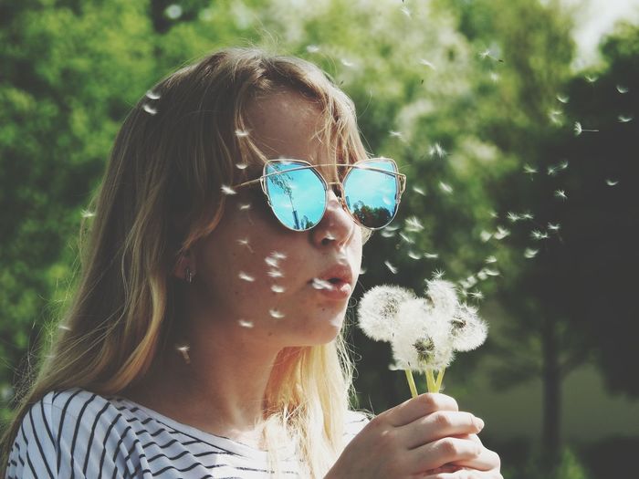 Close-up of girl wearing sunglasses blowing dandelion
