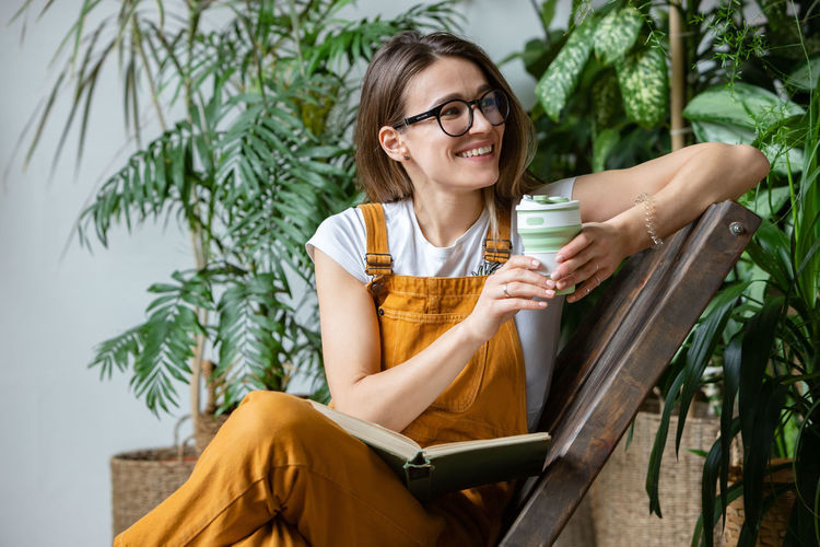 Smiling woman reading book and having coffee while sitting on chair