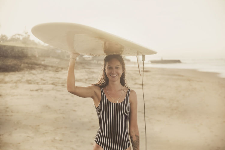 Portrait of happy female surfer carrying surfboard on head at b