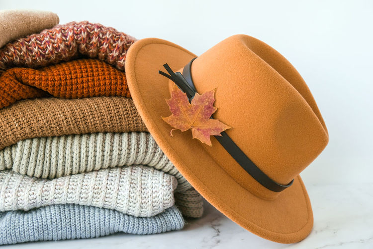 Stack of cozy knitted warm sweater with autumn fall maple leaf and beige stylish hat. sweaters 