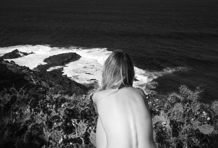 Rear view of shirtless woman looking at sea