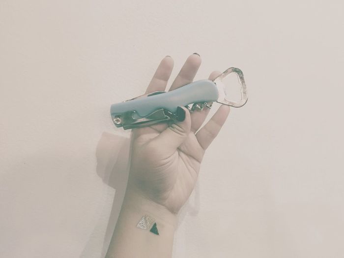 Close-up of cropped hand holding penknife with bottle opener against beige background