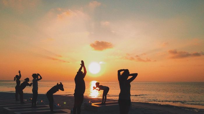Silhouette women exercising on beach by sea against sky during sunset