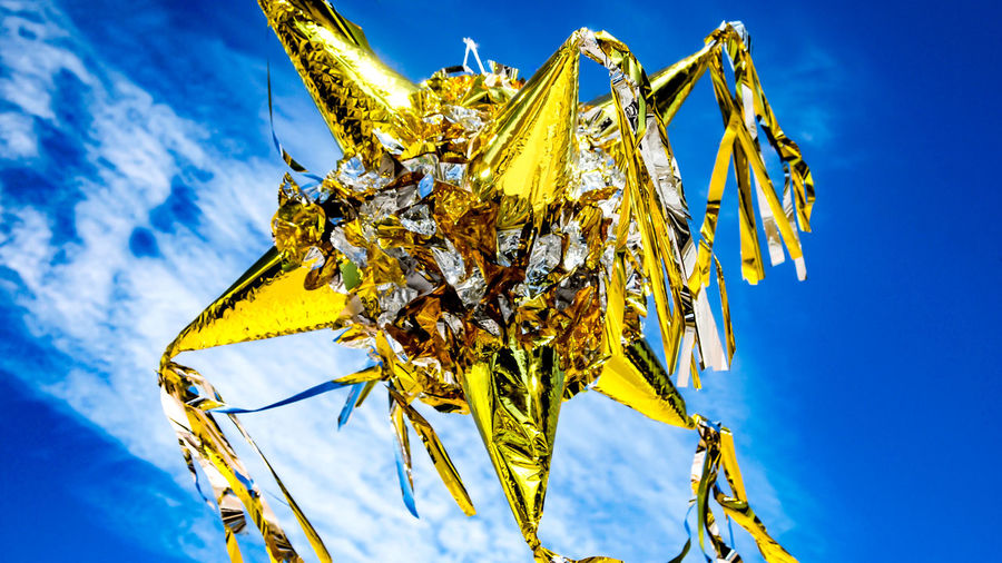 Low angle view of a large gold and silver colored mexican pinata against a blue sky with clouds