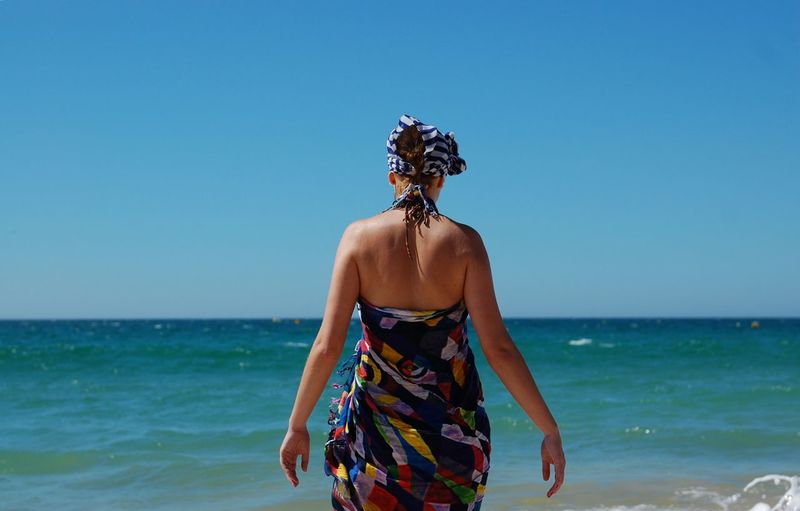 Rear view of person standing at beach against clear blue sky