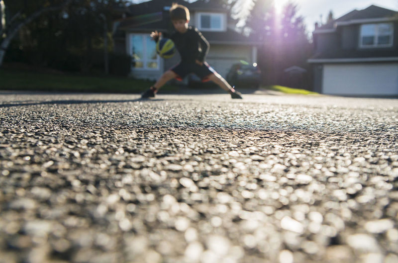 Surface level shot of boy playing with ball on road during sunny day