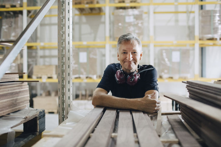 Portrait of smiling worker leaning on wooden planks at industry