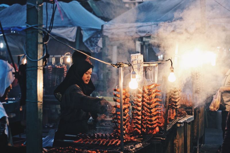 Woman preparing food in market stall at night