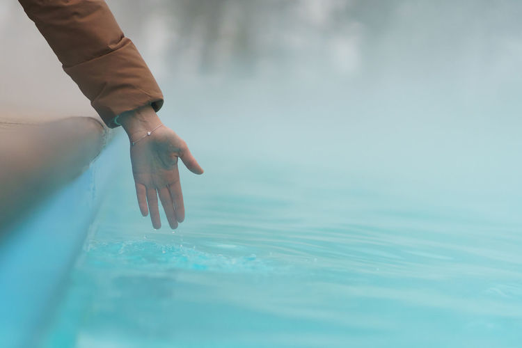 Hand of woman checking temperature of water in open swimming pool in winter. thermal spa outdoors.